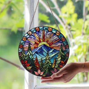 May include: A circular stained glass window, suspended by a chain. It depicts a mountain landscape with a setting sun, trees, and vibrant colours. The glass is a mosaic of blues, oranges, greens, and purples.