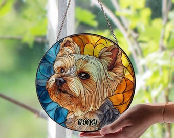 May include: Circular stained glass window decoration with a Yorkshire Terrier dog portrait. The artwork has a black border and a chain for hanging. The dog's name, "Rocky," is written at the bottom. The background is a mix of blue, yellow, and orange.