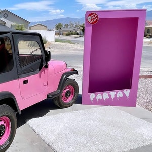 May include: A pink Jeep with a black soft top and black wheels with pink rims. The Jeep is parked in front of a large pink cardboard cutout with the word "PARTAY" written on it in white letters.
