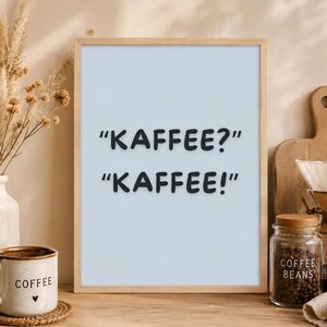 Könnte beinhalten: Ein gerahmter Druck mit den Worten "KAFFEE?" und "KAFFEE!" in Schwarz. Eine Kaffeetasse mit dem Wort "COFFEE" und einem Herz steht auf einem Untersetzer. Ein Glas mit Kaffeebohnen und eine Kaffeemaschine sind ebenfalls zu sehen.