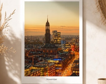 Peut inclure: Un calendrier mural présentant une photographie verticale de l'horizon de Hambourg au coucher du soleil, avec la tour de l'église Saint-Michel bien visible. Le mot November est imprimé en noir sur la bordure blanche sous l'image.