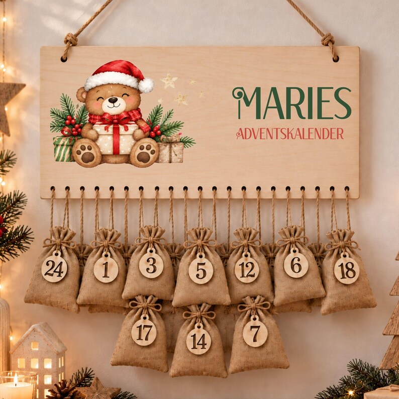 May include: A rectangular wooden advent calendar sign featuring a cartoon teddy bear in a Santa hat holding a gift, with the text MARIES ADVENTSKALENDER. Twenty-four small burlap drawstring bags with numbered wooden tags hang from the sign.