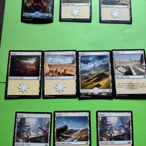 May include: A collection of nine Magic: The Gathering Plains cards, featuring various illustrations of landscapes and cityscapes. The cards are all in good condition and have a white background with black borders.