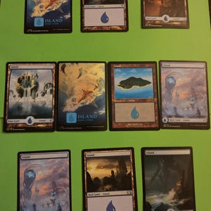 May include: A collection of nine Magic: The Gathering Island cards, each featuring a different illustration of a watery landscape. The cards are all in good condition and have a black border.