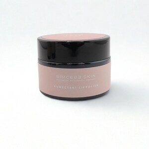 Op de afbeelding: Een ronde pot lipscrub met een zwarte deksel en een lichtroze body. De pot heeft de tekst "SPACEES SKIN" en "HUMECTANT LIP POLISHER" op de body. De pot staat op een witte ondergrond.