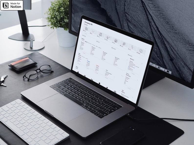 May include: A silver laptop displaying a webpage with a grid of icons and text sits on a black desk. A white keyboard, glasses, wallet, and phone are also on the desk. A monitor and plant are in the background. The text "Made for Notion" is in the top left corner.