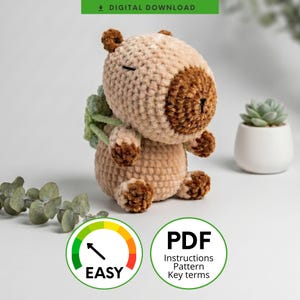 May include: A crochet capybara plush toy made with light tan and dark brown yarn, featuring a small green crocheted plant attached to its back. The toy has closed eyes and a simple stitched nose. The image includes text labels for digital download.