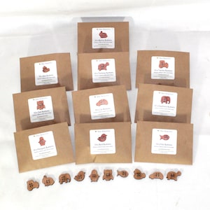 May include: A selection of wooden craft buttons in animal shapes, such as a bee, bunny, tortoise, tractor, owl, car, elephant, penguin, bird, and fish. Each pack contains 10 buttons and is presented in a brown paper envelope.