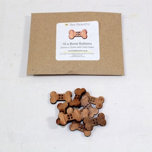 May include: Ten wooden bone-shaped buttons with two holes each. The buttons are 25mm x 15mm and have a natural wood colour. The buttons are packaged in a brown paper envelope with a label that says "Bee Beautiful" and "10 x Bone Buttons 25mm x 15mm with 2mm holes".