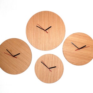 May include: Four wooden wall clocks with black hands and red accents. The clocks are of different sizes and are arranged in a staggered pattern on a white wall.
