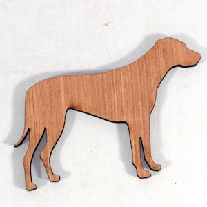 May include: A wooden dog silhouette, standing with its head up. The dog is a light brown colour with visible wood grain. The cutout has a black outline. Likely a decorative item or for crafting, made from wood.