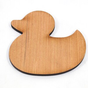 May include: A wooden duck-shaped cutout with a light brown finish and a black edge. The duck has a simple, rounded design, with a beak and a curved body. The wood grain is visible on the surface.