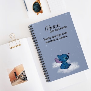 Pode incluir: Um caderno espiralado com capa azul clara com a palavra "Ohana" e texto em português. Um personagem de desenho animado é retratado em uma nuvem. O caderno está aberto, revelando uma página em branco e um clip de papel dourado.