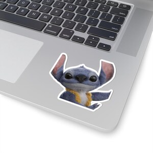 Pode incluir: Um autocolante recortado com a personagem Stitch do filme da Disney Lilo & Stitch. O autocolante mostra Stitch com as suas orelhas grandes, pelo azul e uma gola amarela. O autocolante está colocado num portátil.