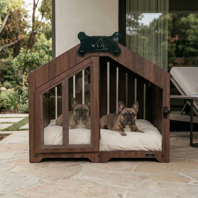 Two French bulldogs lying comfortably inside the Walnut WLO dog house placed on a stone patio, with garden plants and outdoor furniture in the background, showing covered outdoor use.