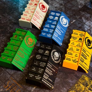 Può includere: Cinque tabelloni segnapunti rettangolari in bianco, blu, verde, nero e giallo. Ogni tabellone presenta un coperchio incernierato con un emblema di teschio e alloro e una griglia di pulsanti etichettati per tracciare le statistiche di gioco.
