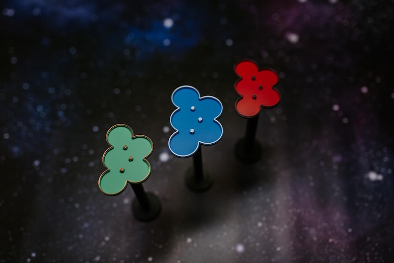 May include: Three colorful, flower-shaped decorative objects on black stems. The objects are green, blue, and red, each with three small, white dots. The background is a dark, starry space.