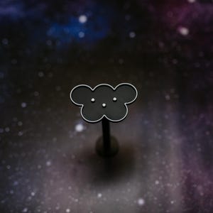 May include: A black cloud-shaped pin with a silver outline and three small white dots, set against a dark, starry background. The pin is mounted on a thin, dark post. The design is simple and elegant.