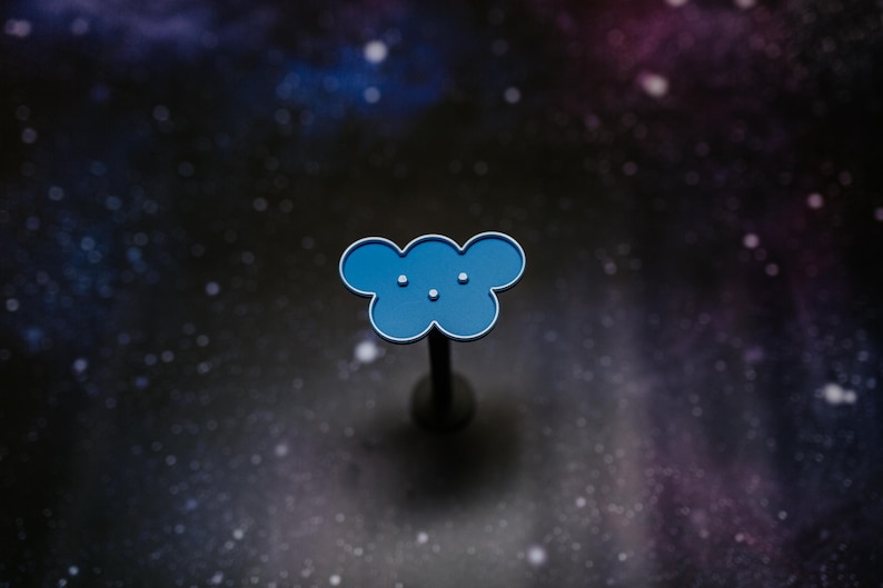 May include: A blue cloud-shaped pin with a silver outline and three small white dots. The pin is mounted on a dark gray post. The background is a dark, starry space scene.