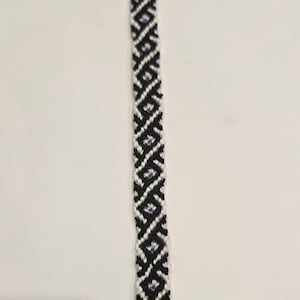 May include: A black and white friendship bracelet with a purple and white diamond pattern.