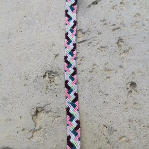 May include: A multi-coloured friendship bracelet with a chevron pattern in shades of pink, green, purple, and brown.