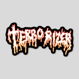 May include: A black and white sticker with the word "TERRORIZER" in a dripping, stylized font. The letters are outlined in orange and red, creating a gradient effect.