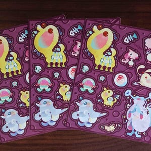 May include: Four sheets of stickers with a purple background and various colorful cartoon characters. The characters include a yellow dog, a blue fish, a pink and white cat, and a purple octopus.