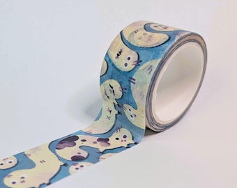 May include: A roll of decorative washi tape featuring a repeating pattern of pale yellow, worm-like creatures with dark eyes and small limbs against a blue background. The tape is partially unrolled, showing the continuous illustrated design.
