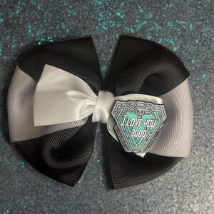 May include: A handmade hair bow featuring black, gray, and white ribbon. The bow is accented with a white satin knot and a decorative pin that reads "I LOVE YOU 3000" in teal and white.