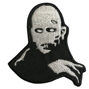 May include: Black and white embroidered patch of a zombie with a stitched-up mouth and a menacing expression.