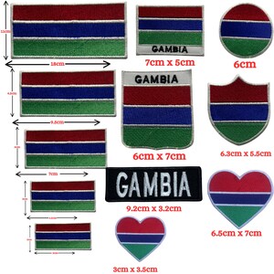 May include: A collection of embroidered patches featuring the flag of Gambia in various shapes and sizes. The patches include rectangular, circular, shield, and heart shapes, with dimensions ranging from 3cm x 3.5cm to 18cm x 11cm. The word "GAMBIA" is embroidered on some patches.
