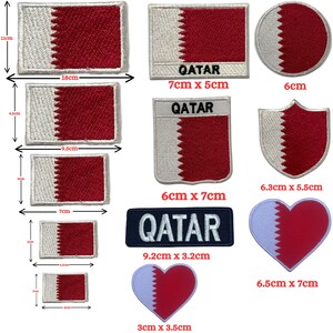 Puede incluir: Una colección de parches bordados con el diseño de la bandera de Qatar. Se muestran varias formas y tamaños, incluyendo parches rectangulares, circulares y en forma de corazón. Los parches tienen colores blanco y granate, con la palabra "QATAR" en algunos.