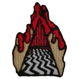 May include: Embroidered patch featuring a red and black triangle with a zigzag pattern at the base. The top of the triangle has red flame-like details. The patch has a tan border and is likely for clothing or accessories.