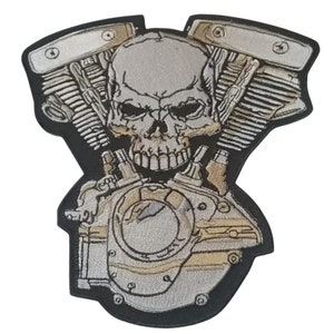 May include: A silver and black embroidered patch of a skull with a motorcycle engine behind it.