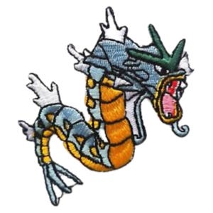 May include: Embroidered patch featuring a stylized dragon-like creature with a light blue body, orange belly, and green accents. The patch has white details and a red mouth, perfect for adding to clothing or accessories.