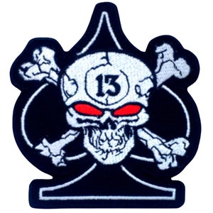May include: Black and white embroidered patch with a skull and crossbones design. The skull has red eyes and the number "13" on its forehead. The skull is centered on a black ace of spades.