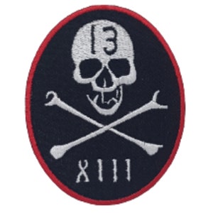 May include: A black and white embroidered patch with a skull and crossbones. The skull has the number "13" on its forehead and the number "XIII" below the crossbones.