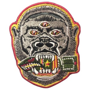 Puede incluir: Parche bordado con un gorila gris de tres ojos, boca roja y una granada verde y amarilla en los dientes.