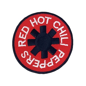 Puede incluir: Parche bordado circular con la inscripción "RED HOT CHILI PEPPERS" en blanco sobre fondo rojo. Un símbolo negro en forma de asterisco se encuentra en el centro. Ideal para personalizar ropa y accesorios.
