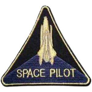 Può includere: Toppa triangolare con bordo e sfondo neri. La toppa presenta un disegno di space shuttle color oro sopra le parole "SPACE PILOT" in lettere bianche su sfondo blu. La toppa è probabilmente per un'uniforme o una giacca.
