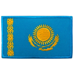 Może przedstawiać: Naszywka haftowana przedstawiająca flagę Kazachstanu. Flaga jest niebieska z  złotym słońcem w środku, otoczonym promieniami i stylizowanym orłem.