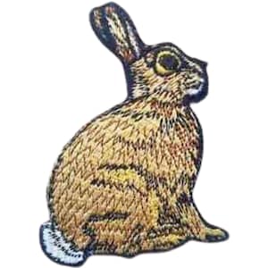 以下が含まれることがあります： 茶色と白の刺繍でできた、座って耳を立てたウサギのアップリケです。