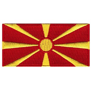 May include: A red embroidered patch with a yellow sun and rays, representing the flag of North Macedonia.
