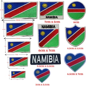 May include: A collection of embroidered patches featuring the flag of Namibia in various shapes and sizes. The patches include rectangular, circular, and heart-shaped designs, with the word "NAMIBIA" on some. The flag design includes blue, red, green, and a yellow sun.