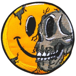 May include: A yellow smiley face with a cracked design, half of which is replaced with a gray skull. The skull has white teeth and black eyes.