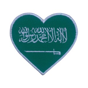 Puede incluir: Parche verde en forma de corazón con escritura árabe bordada en blanco y una espada blanca. El parche es una representación de la bandera de Arabia Saudita.