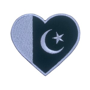 Puede incluir: Un parche en forma de corazón verde y blanco con la bandera de Pakistán. La bandera presenta una luna creciente blanca y una estrella de cinco puntas sobre un fondo verde.