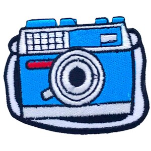 Pode incluir: Um remendo bordado azul e branco de uma câmera vintage com um botão de obturador vermelho. A câmera tem uma alça branca.
