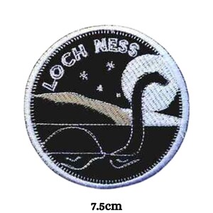 May include: A black and white embroidered patch with the text "LOCH NESS" in white. The patch features a stylised image of the Loch Ness Monster, a mythical creature, in the water with stars in the sky. The patch is 7.5 cm in diameter.