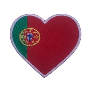 Puede incluir: Un parche rojo en forma de corazón con un contorno blanco. El parche presenta la bandera portuguesa, con un fondo verde y rojo y el escudo de armas portugués en el centro.
